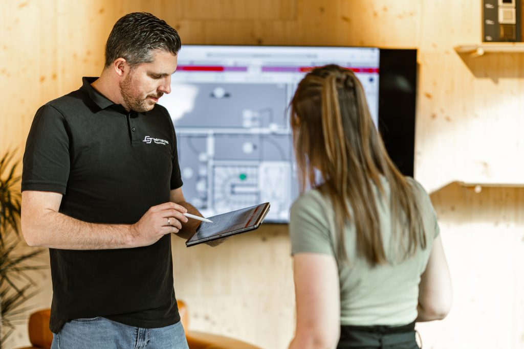 Elektromeister von Schöttler & True zeigt einer Kundin die Smart-Home-Visualisierung am Tablet